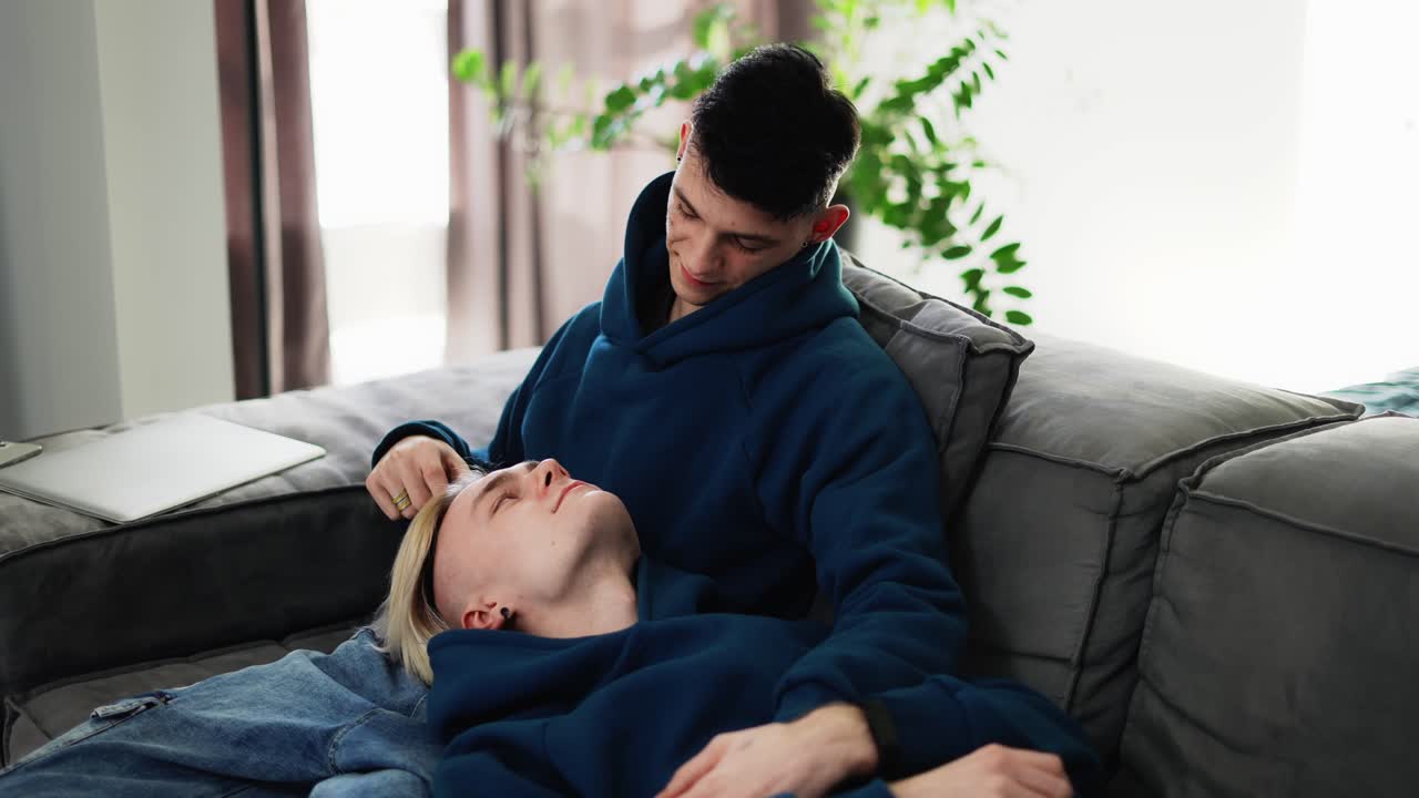 Gay male couple relax on couch, embracing, talking to each other