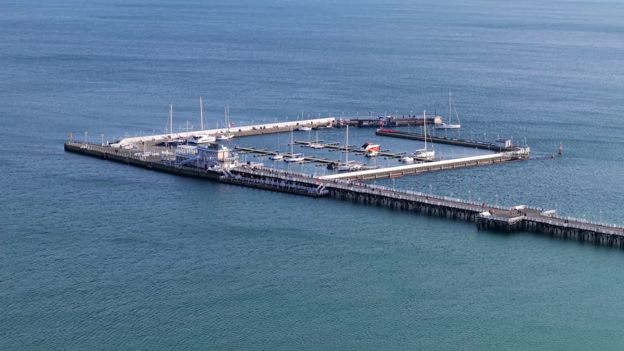 Aerial winter orbit of Sopot Pier, Marina, beach, and boats leaving the harbor, calm empty blue ocean water