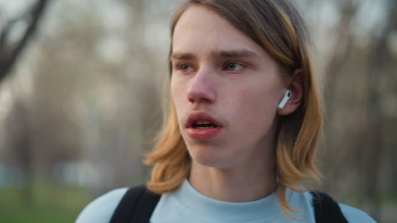 Ragazzo/a sorseggia tranquillamente una bevanda all'aperto, giovane rilassato/a con auricolari che tiene in mano un caffè in un parco tranquillo, teenager che sorseggia tranquillamente un caffè mentre ascolta musica con gli auricolari in un parco all'aperto