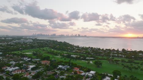 Foto-Romántica-De-Un-Barrio-Residencial-De-Lujo-Y-Un-Campo-De-Golf-Frente-Al-Mar.-Horizonte-Con-Rascacielos-Contra-El-Cielo-Del-Atardecer-En-La-Distancia.-Miami,-Estados-Unidos