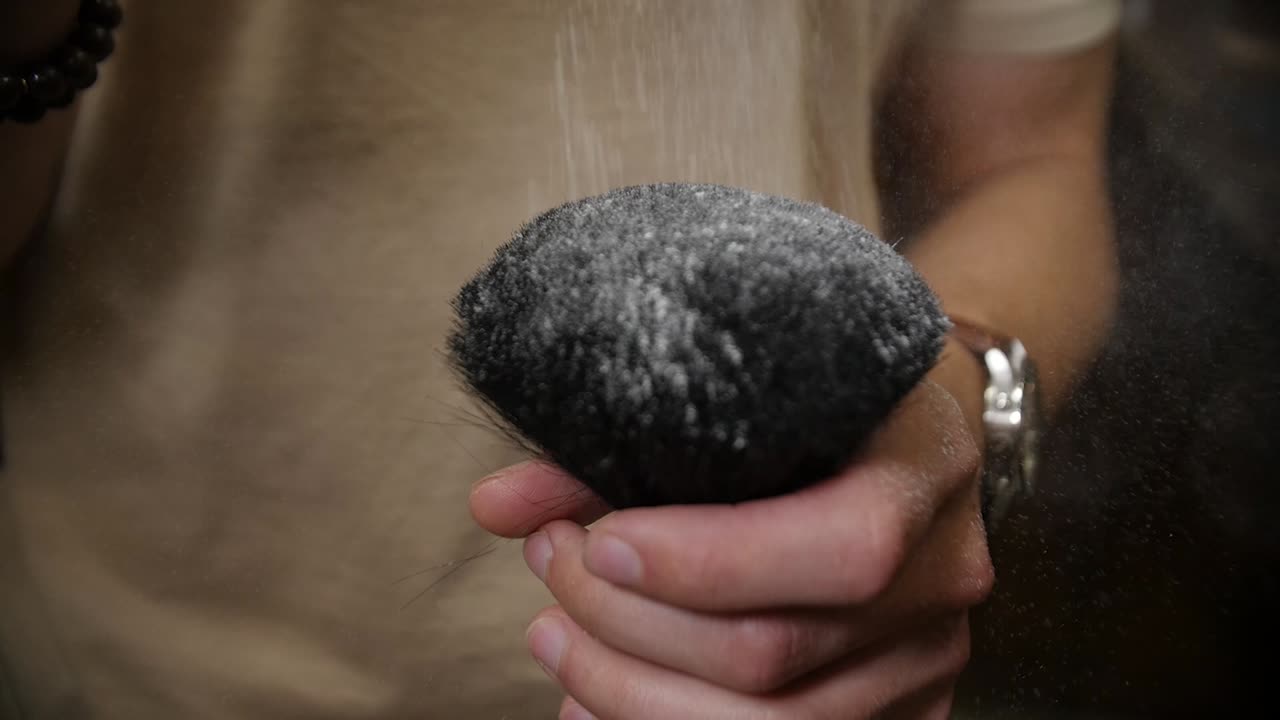 이발사는 브러시에 천천히 떨어지는 헤어 파우더를 뿌리고 주위에 뿌립니다.