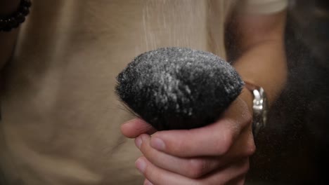 the barber sprinkles hair powder which slowly falls on the brush and is sprayed around