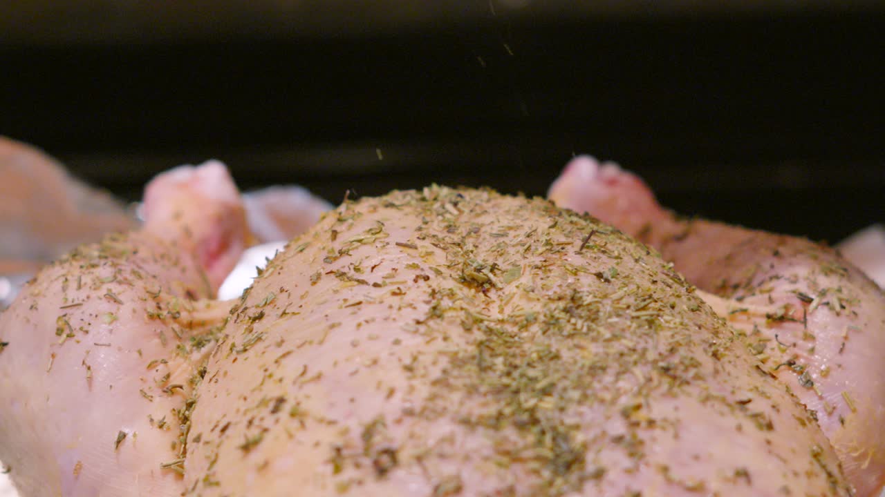 Herb Seasoning Gently Falling on Raw Whole Free Range Chicken in Slow Motion with Legs Visible Ready to Roast For Dinner. Cooking Food Footage 4K.