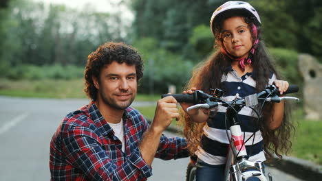 closeup. portrait of a little girl and her dad next to the bike. looking into the camera. smiling. blurred background