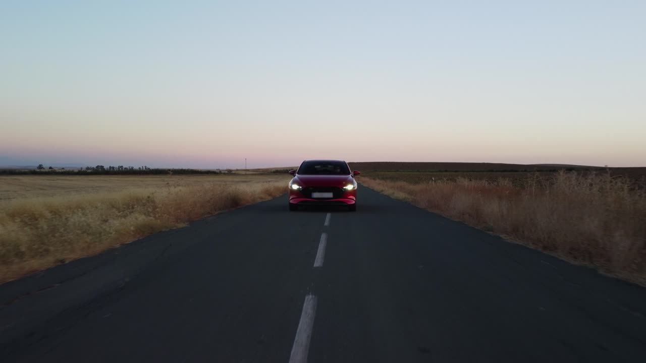 Low POV : Shiny red vehicle drives on country road at dawn, headlights