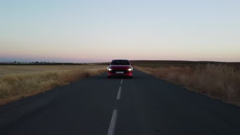 low pov : shiny red vehicle drives on country road at dawn, headlights