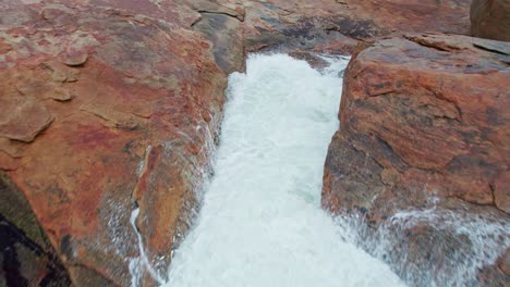 impresionante toma aérea de bajo nivel de una costa rocosa con grandes olas verdosas rompiendo en las rocas