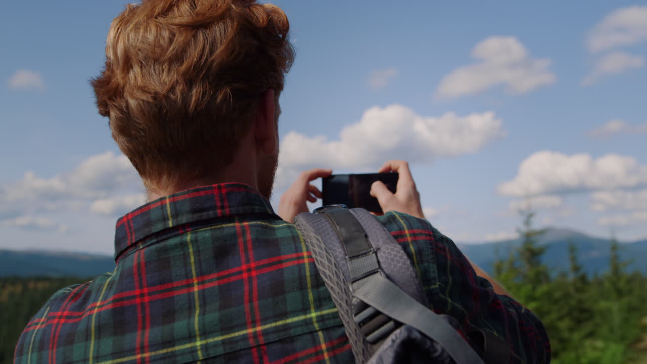 젊은이가 휴대 전화로 여름 산의 비디오를 만들고 있습니다.