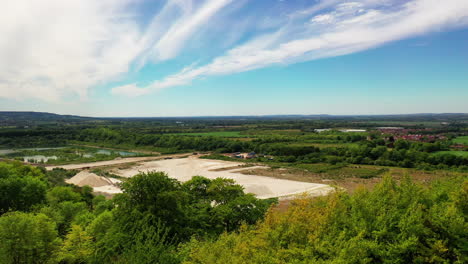 Aerial-shot-rising-above-tree-tops-to-reveal-quarry,-on-bright-sunny-day