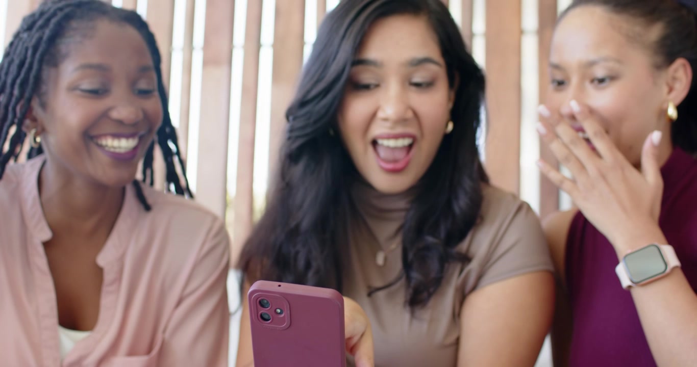 Diverse female friends watching center woman tapping mauve smartphone, sharing content on bench