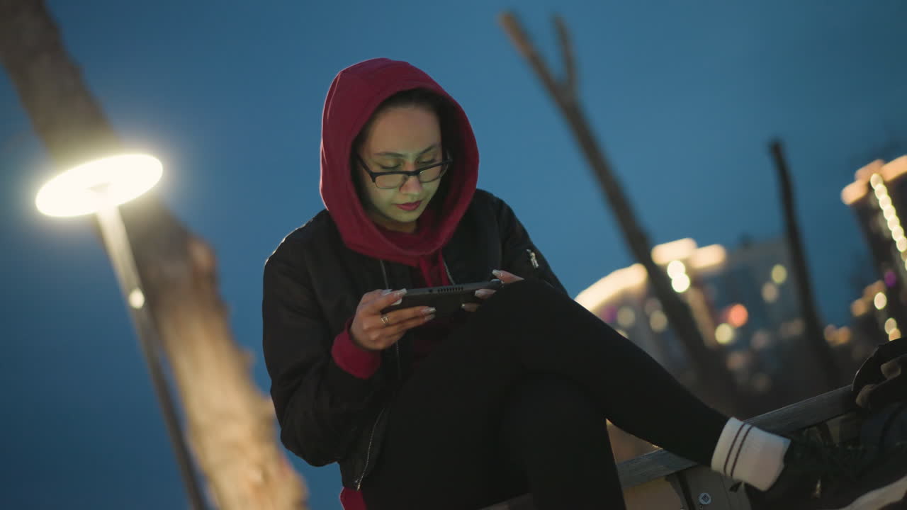 Intense Gaming Action Against City Background, Player Intensely Engaged With Mobile Device Beneath City Lights, Focused Gamer Immersed In Lively Cityscape Illuminated By Vibrant Lights
