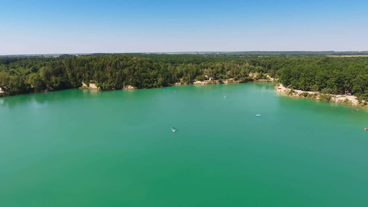 Beautiful scenery of a blue lake surrounded by rocky bank with green forests. Blue skies reflecting in the water. Aerial view.