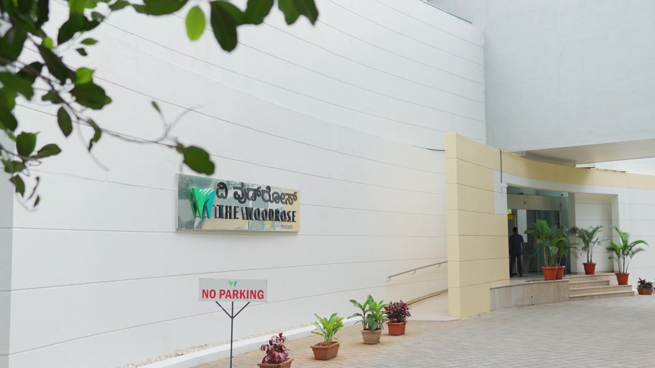 Vista exterior en cámara lenta de la entrada de un club moderno con plantas en maceta y señalización.