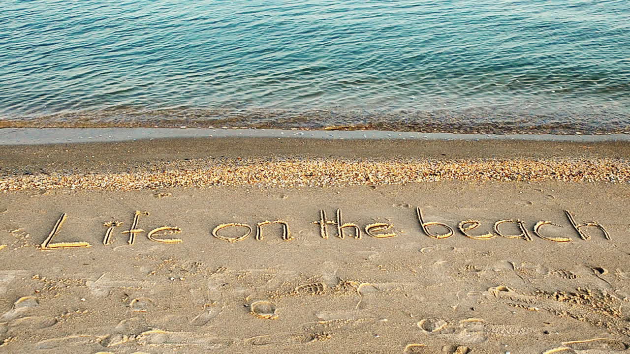 Optagelse på stranden. Livet på stranden-koncept – inskription i strandsand med en kommende bølge.