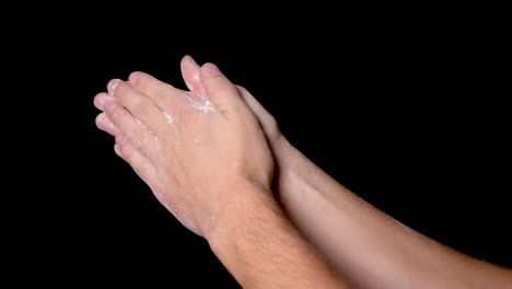 an athlete preparing for workout by clapping his hands for evenly distributing the chalk powder, isolated on black background