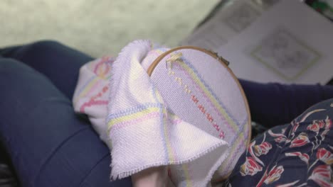 establishing shot of a woman cross-stitching a pattern under a craft lamp