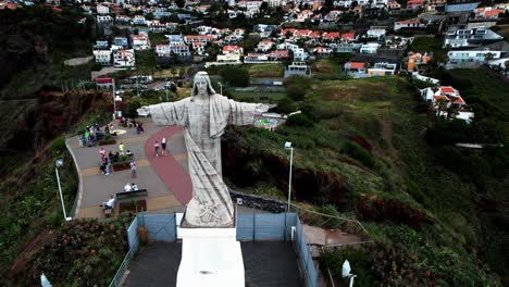 Aerial-view-orbiting-Cristo-Rei-monumental-statue-overlooking-Madeira-coastline-from-island-hillside