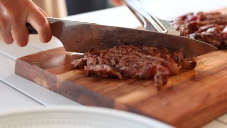 chef slices beef steak on a wooden board with a sharp knife. bright kitchen setting enhances focus on culinary skill