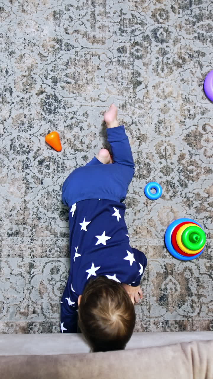 Baby boy trying to reach under the sofa. Kid plays on the floor indoors. Top view perspective. Vertical video