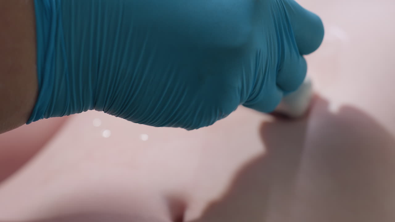 Woman lab technician wearing blue gloves gently moves ultrasound scan probe on patient's abdomen during examination, focusing on accuracy and precision while gel is visibly applied to smooth body