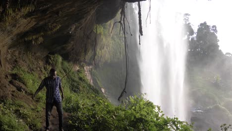 hombre africano caminando en una cueva detrás de una cascada tropical