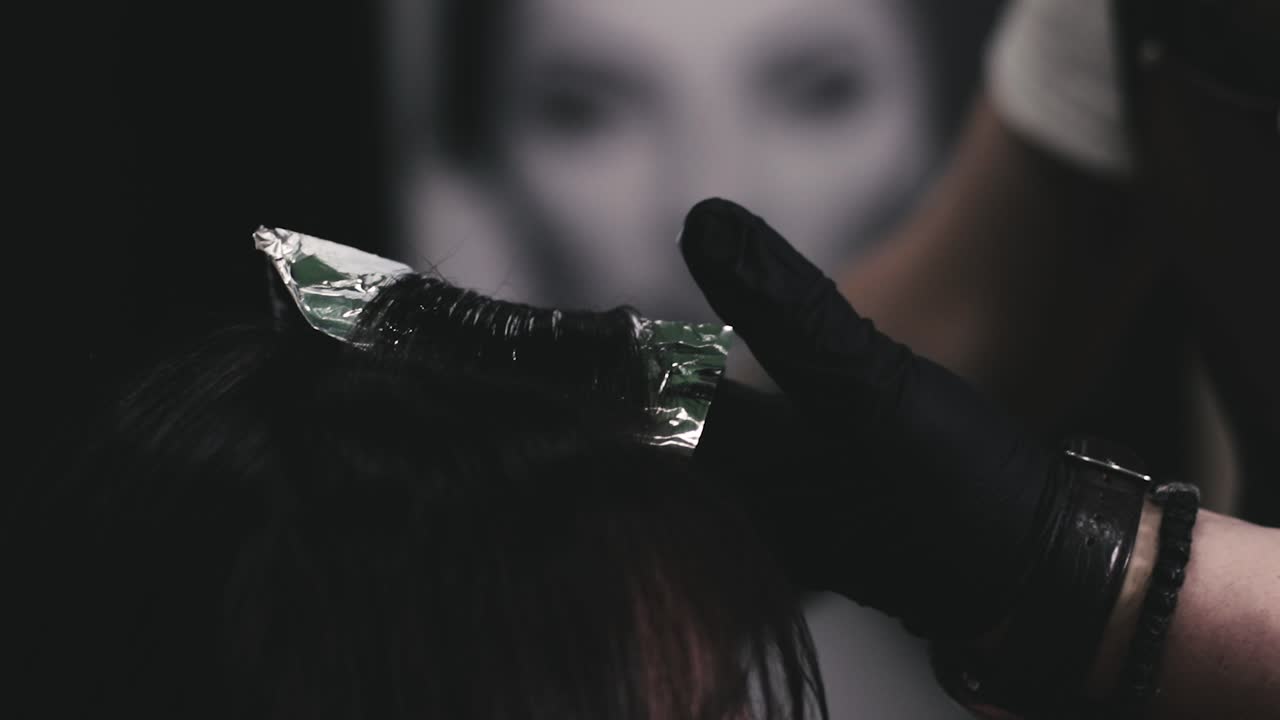 Hair stylist che applica la tinta sui capelli di una donna in un salone di parrucchieri professionale