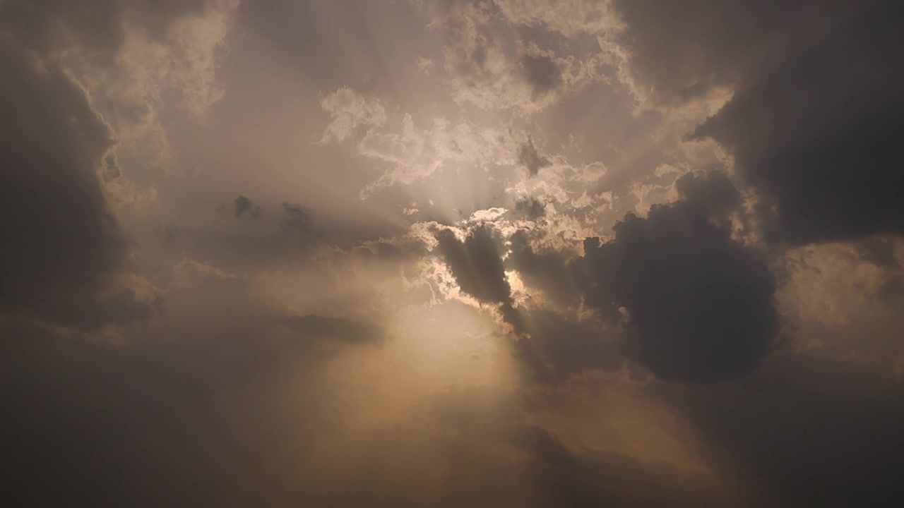Timelapse drammatico di luce solare che penetra attraverso nuvole temporalesche con raggi cinematografici e cielo luminoso, ideale per progetti visivi su meteo, spiritualità, speranza, natura e atmosfera.