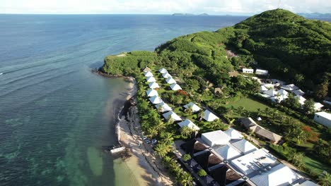 midday aerial pullback over beachfront bungalows and clear water at tokoriki island, fiji