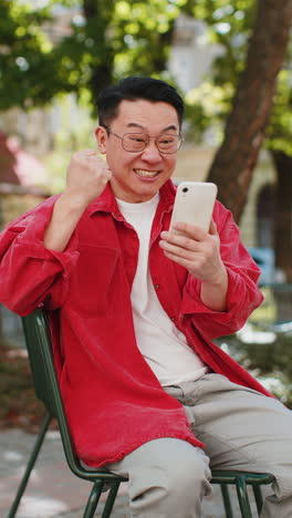 asian man use mobile smartphone celebrating win good message news outdoors on urban city street