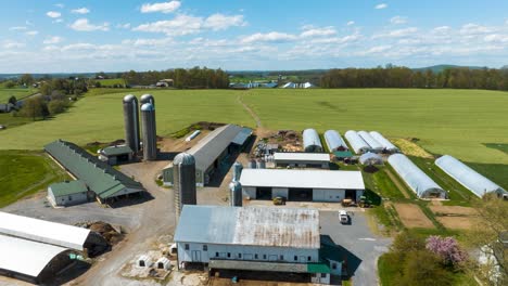 Amerikanischer-Bauernhof-Mit-Mehreren-Gebäuden-Und-Silos,-Umgeben-Von-üppigen-Grünen-Feldern-Im-Frühling