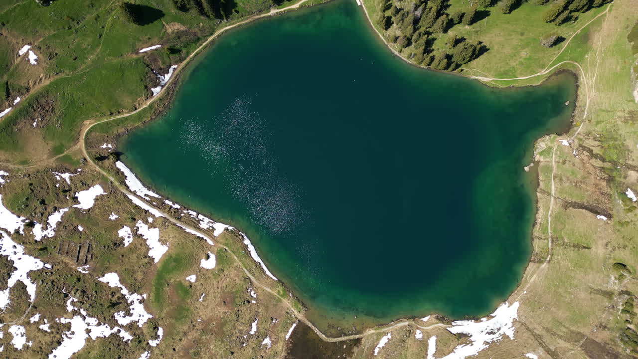 Spiral top down drone shot of Lake Lioson with snow during the day in Ormont-Dessous, near Les Mosses, in the canton of Vaud, Switzerland