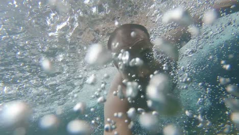young man swimming in blue crystal clear under water with many air bubbles of waterfall
