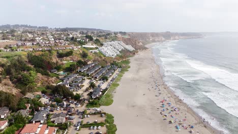 vista aérea de un dron capturando una comunidad costera densamente poblada con casas y una playa esparcida de visitantes en maitencillo, chile
