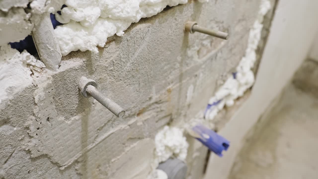A close up shot of an aged threaded concrete screw and plastic plug fixed into a bathroom wall, tiles have been removed and the wall left bare as the shower undergoes maintenance