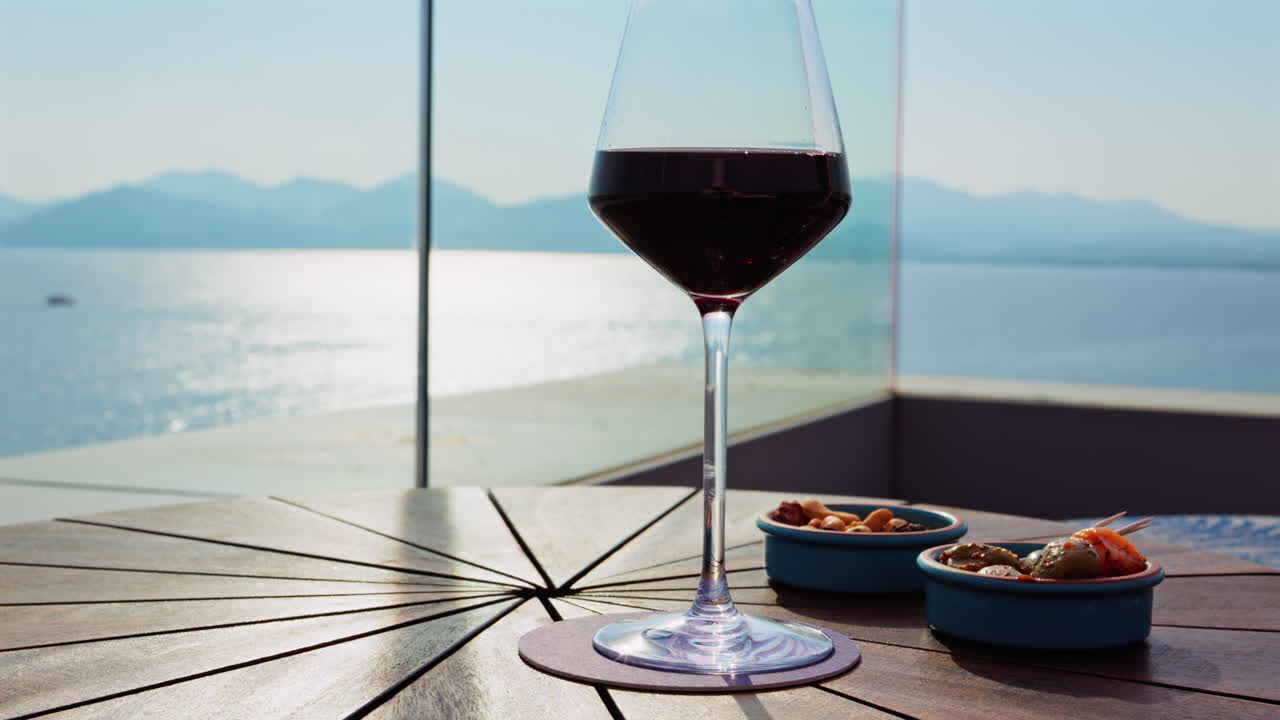 Close up of a glass of red wine and snacks on a table at a terrace with a sea view