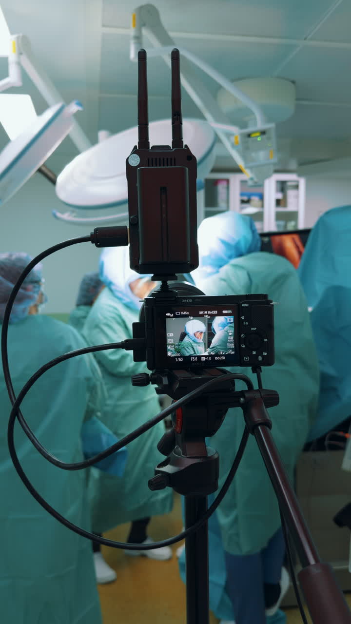 Kyiv, Ukraine, 2 August 2025: Vertical shot of a camera filming a surgical procedure in a brightly lit operating room. The foreground features the camera setup, clearly recording the blurred surgical team in the background