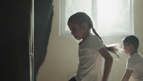 Child girl jumps kicking punching bag in junior gym. Schoolgirl turns doing exercises with fighting inventory in martial arts club slow motion. Self defence