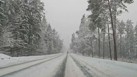 Vista-Del-Parabrisas-Mientras-Conduce-A-Través-De-Un-Hermoso-Camino-Cubierto-De-Nieve-Rodeado-De-Bosques-De-Coníferas-Durante-El-Frío-Día-De-Invierno