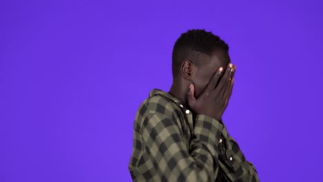 younf african-american man feeling fear isolated on blue background. covers his face with hands in a fear, scary of something