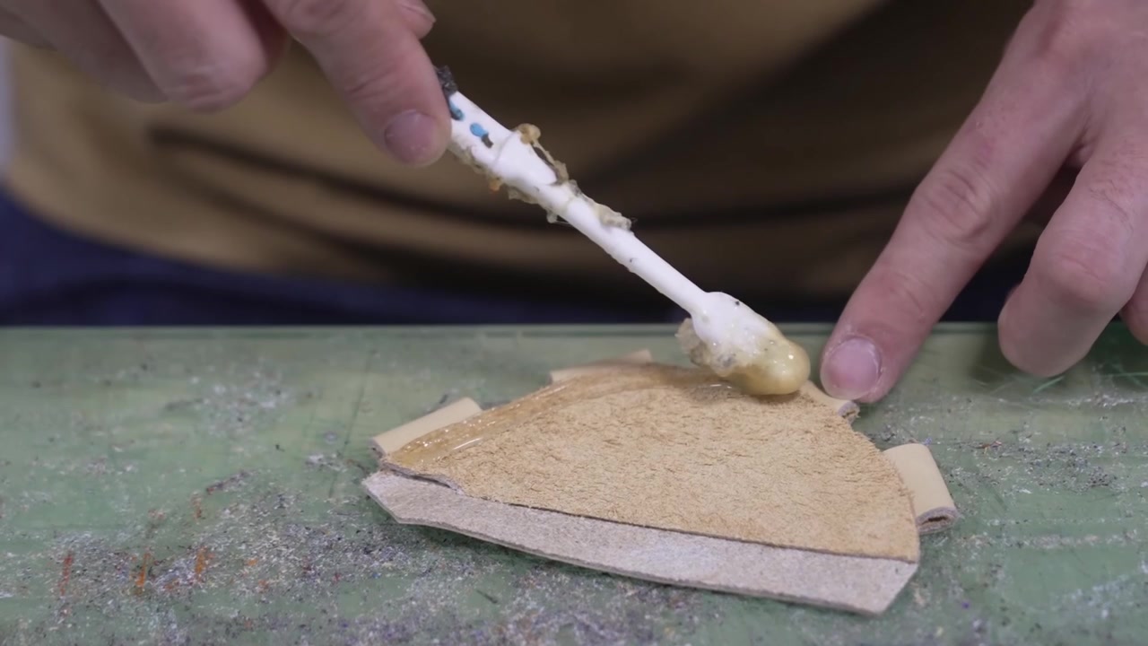 Worker brushing adhesive glue onto a suede leather piece on the workshop bench