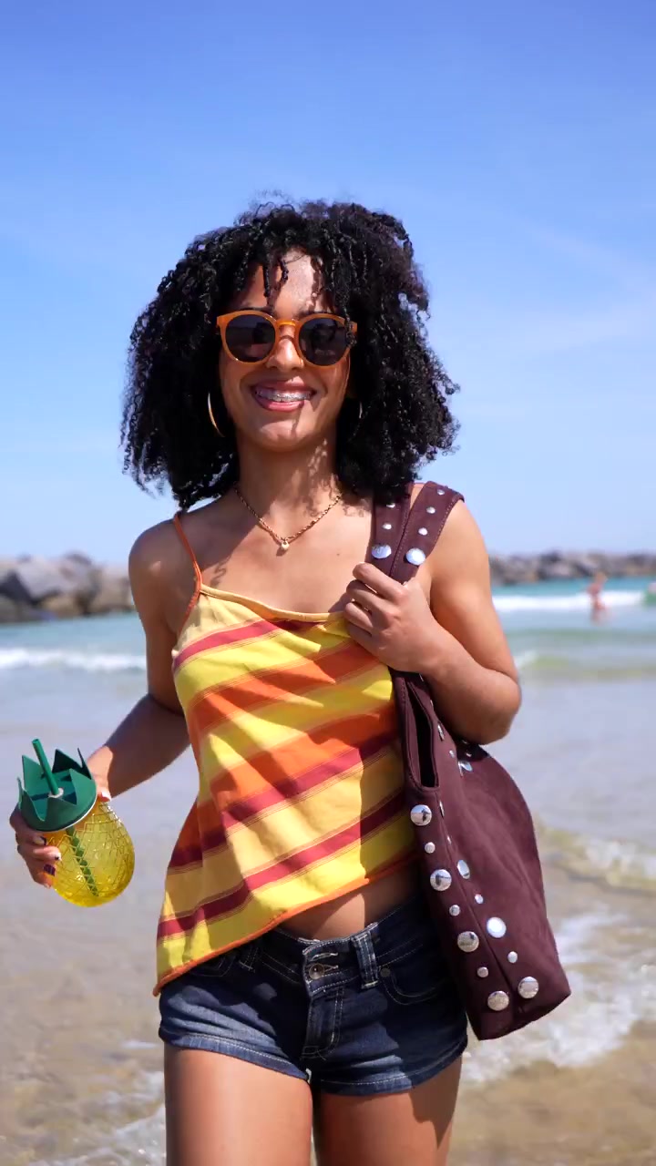 Giovane donna allegra con drink all'ananas che passeggia su una spiaggia assolata