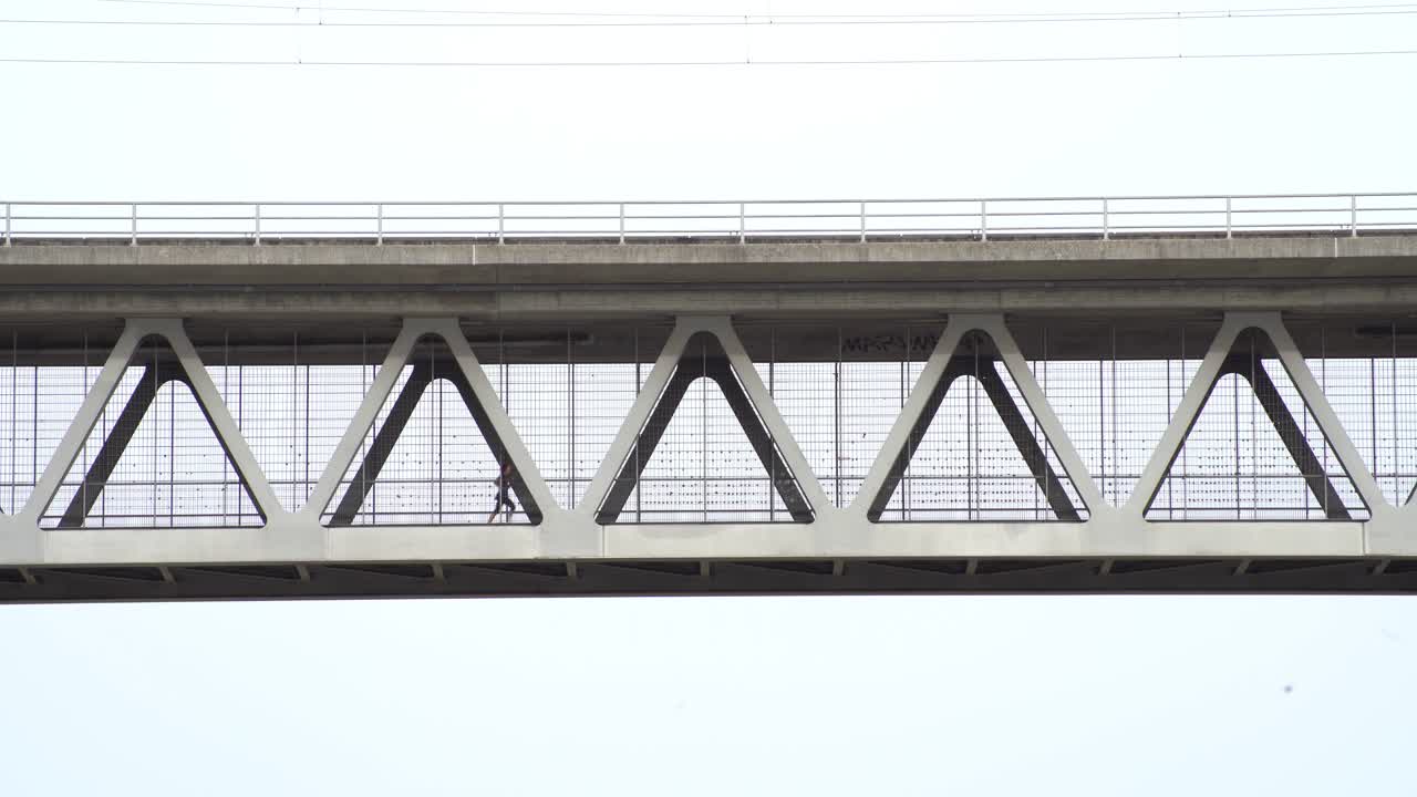 금속 다리에서 왼쪽에서 오른쪽으로 조깅하는 여자, 멀리서 낮은 관점에서 촬영