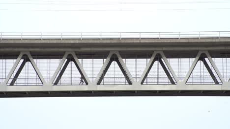 jogging woman from the left to the right at a metal bridge , shot from far away and lower perspective