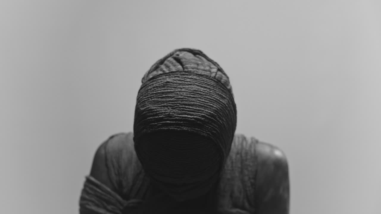 A mummy of a woman on a white backdrop rises her head