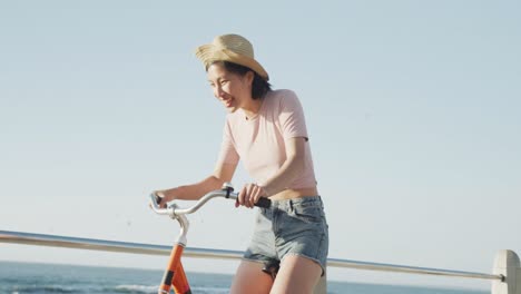 happy biracial woman riding bike on promenade, in slow motion