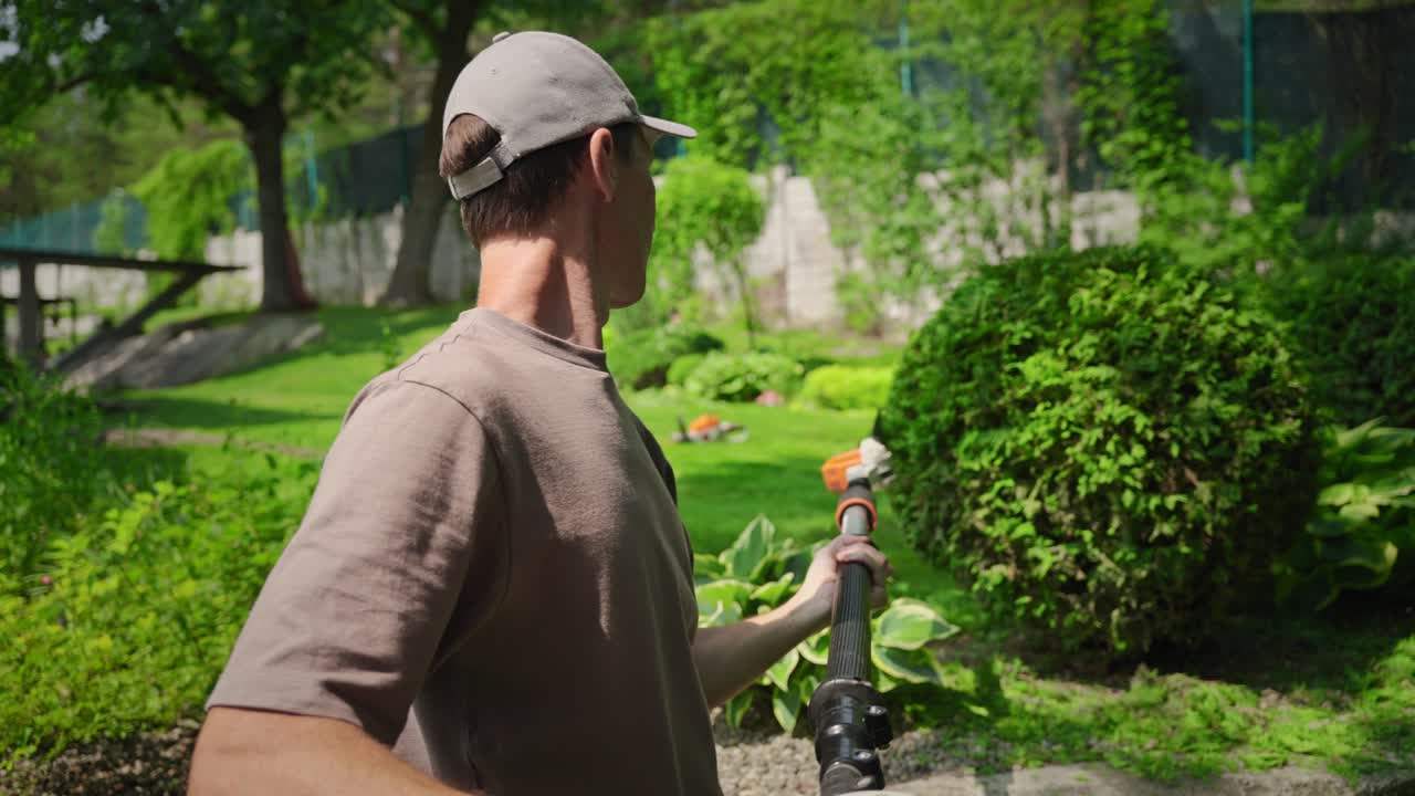 Man Preparing to Trim Bushes with a Long-Handled Hedge Trimmer in Garden