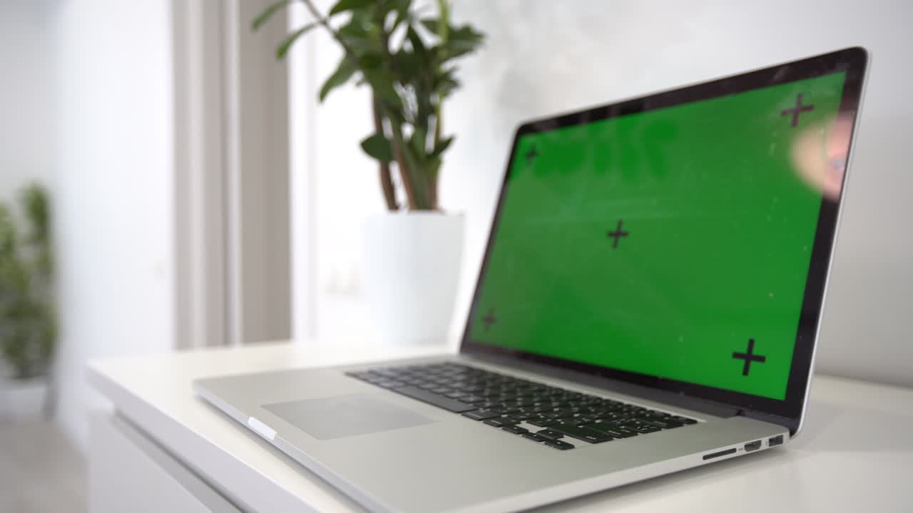 Green screen laptop computer sitting on a home work desk next to a desk lamp.