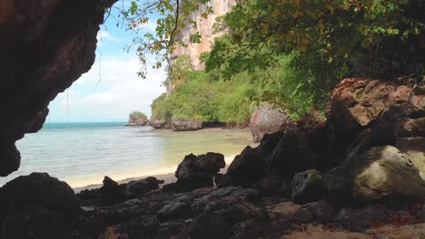 Rai-Island-Beach-in-Thailand,-near-Hong-Island,-Monkey-Island,-Phuket-and-Krabi---Beautiful-Turquoise-Aqua-Emerald-Water,-Golden-Sand,-Rocky-Landscape-Foreground,-Green-Trees,-Blue-Sky-Clouds,-Cliff