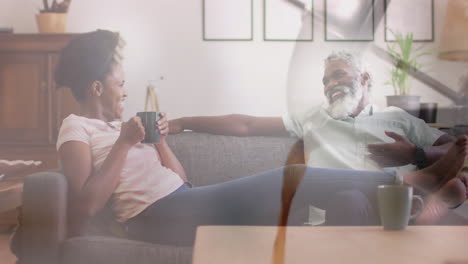 animation of coffee over african american couple sitting on sofa, slow motion