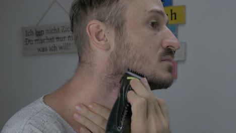 A-Caucasian-male-is-trimming-his-facial-hair-with-an-electric-shaver-to-look-gentle,-The-close-up-footage-shows-a-man's-face-while-he-is-trimming-and-shaving-his-beard